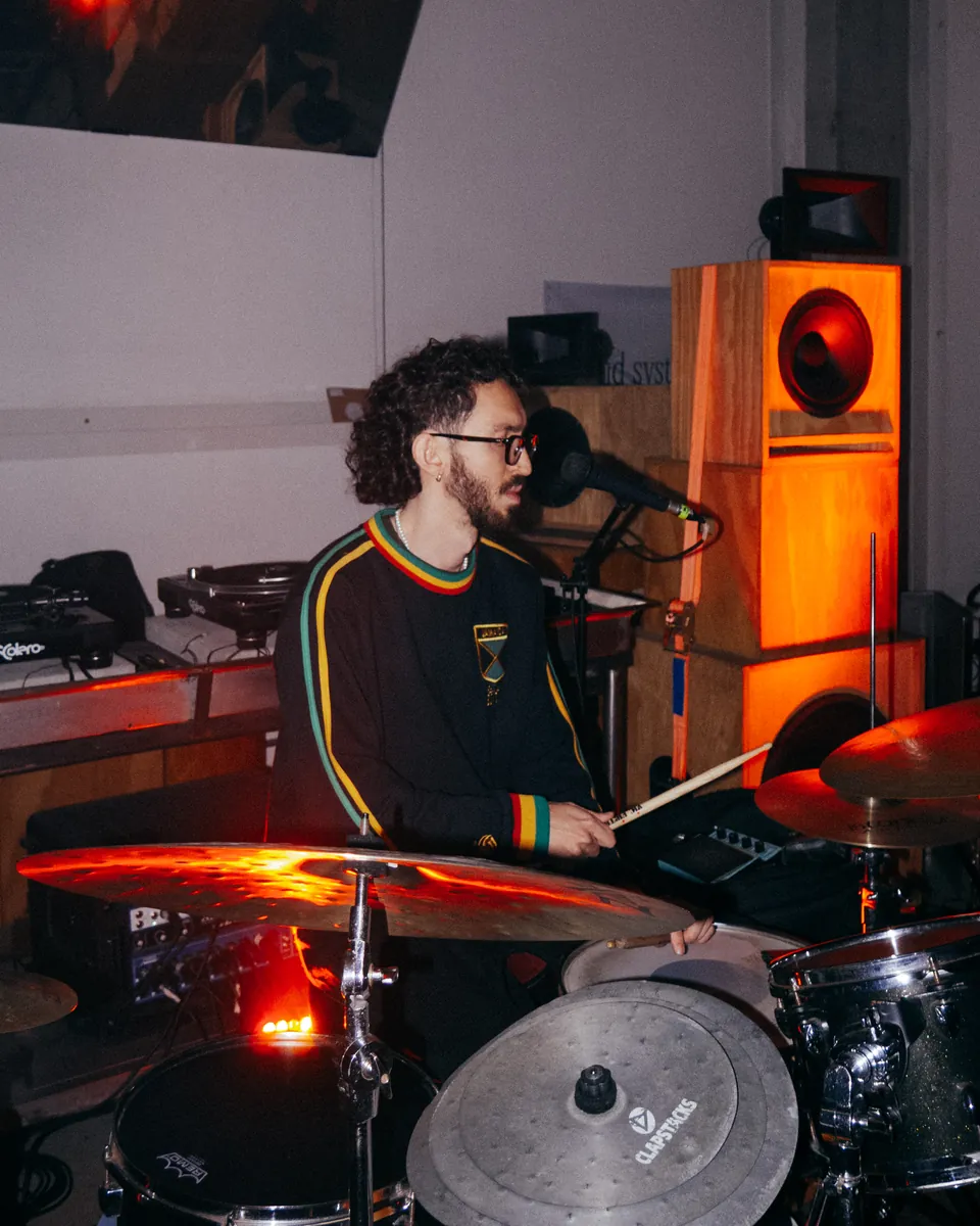 Baterista em apresentação intimista, entre microfone e pratos.