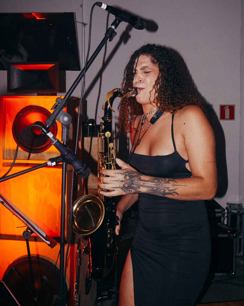 Saxofonista ao lado de um microfone e uma caixa de som iluminada.