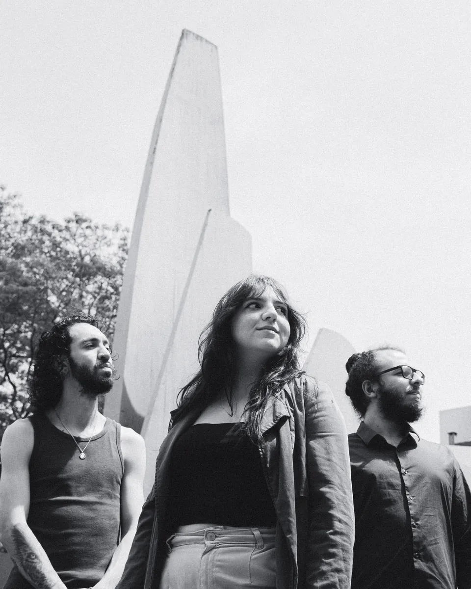 Lima O Trio junto a uma estrutura de concreto, em preto e branco.