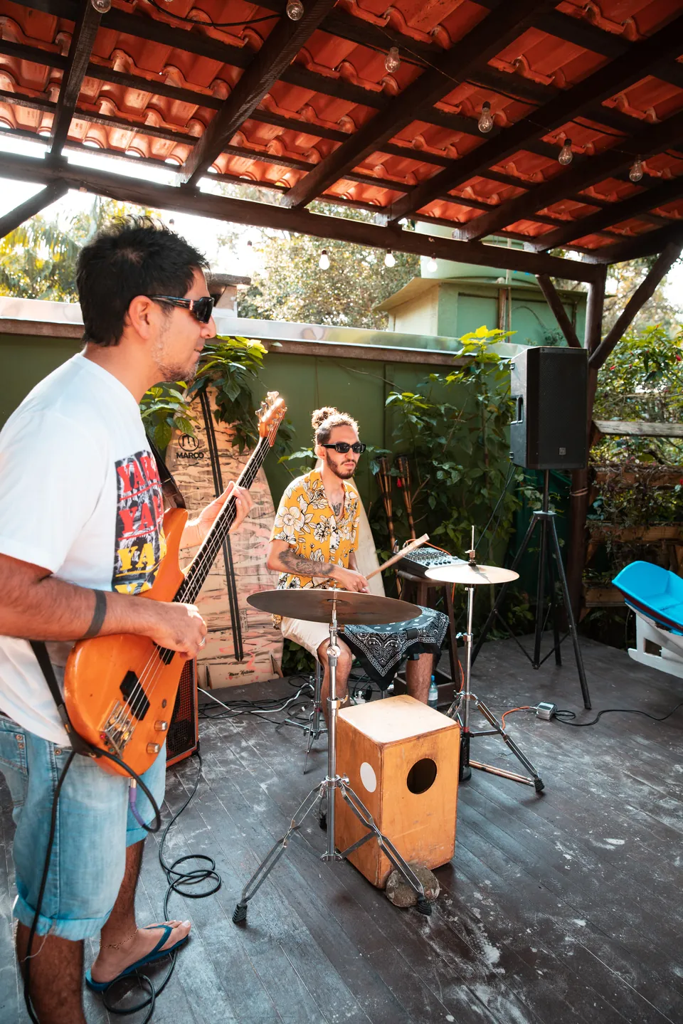 Baixista e baterista de Los Mudos tocando sob um telhado de madeira.